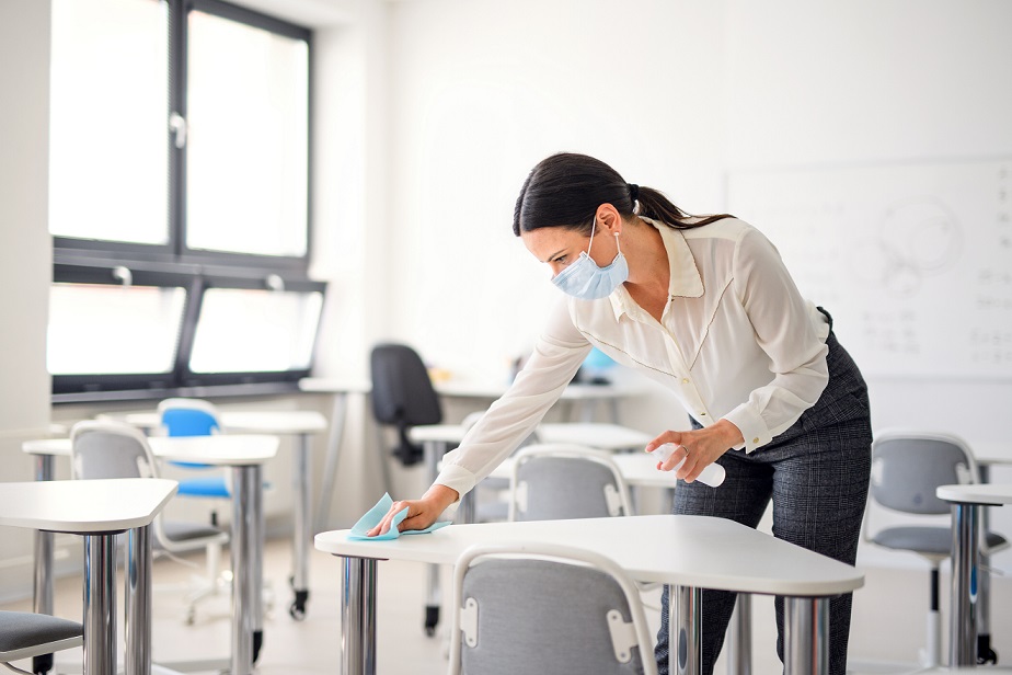 Teacher back at school after covid-19 quarantine and lockdown, disinfecting desks at break time.